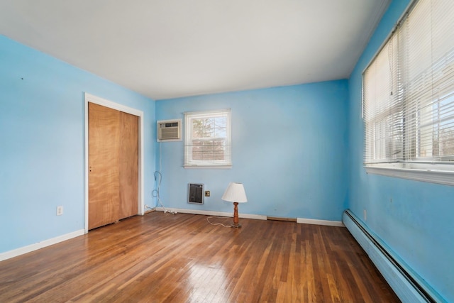 unfurnished bedroom featuring a closet, heating unit, baseboard heating, a wall mounted air conditioner, and dark wood-type flooring