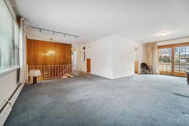 unfurnished living room with a baseboard heating unit, wood walls, carpet floors, rail lighting, and a chandelier