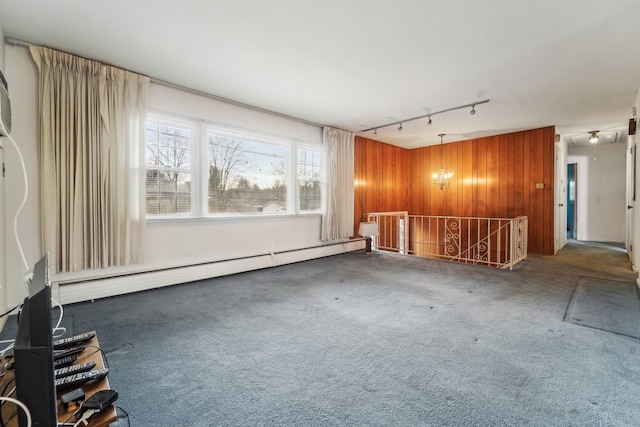 spare room with rail lighting, a baseboard heating unit, wood walls, and dark carpet