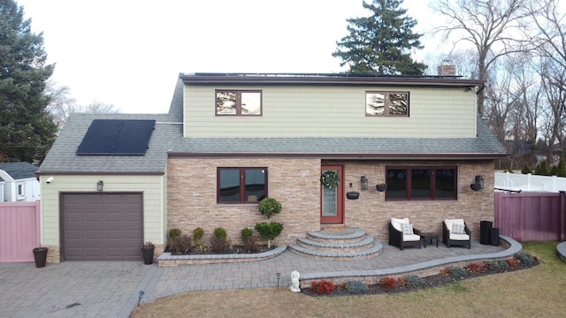 view of front of property featuring a garage, decorative driveway, roof with shingles, roof mounted solar panels, and a chimney