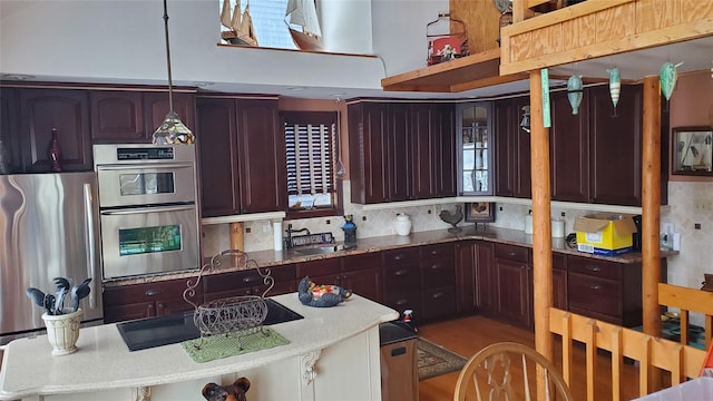 kitchen featuring sink, hanging light fixtures, light stone counters, backsplash, and appliances with stainless steel finishes