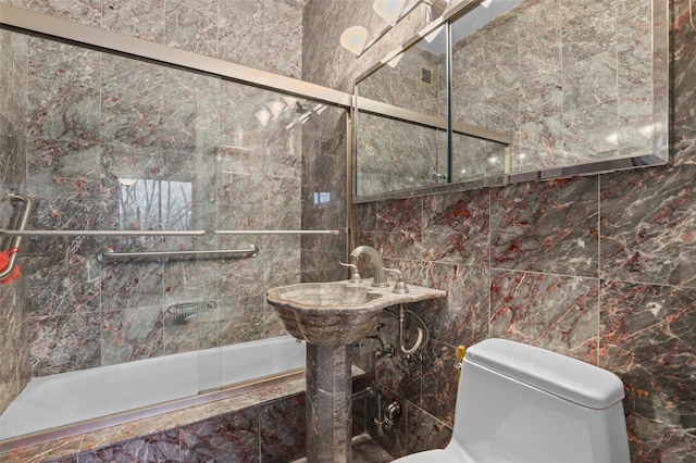 full bathroom with tile walls, sink, bath / shower combo with glass door, and toilet