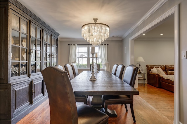 dining room featuring light wood-type flooring, a notable chandelier, and crown molding