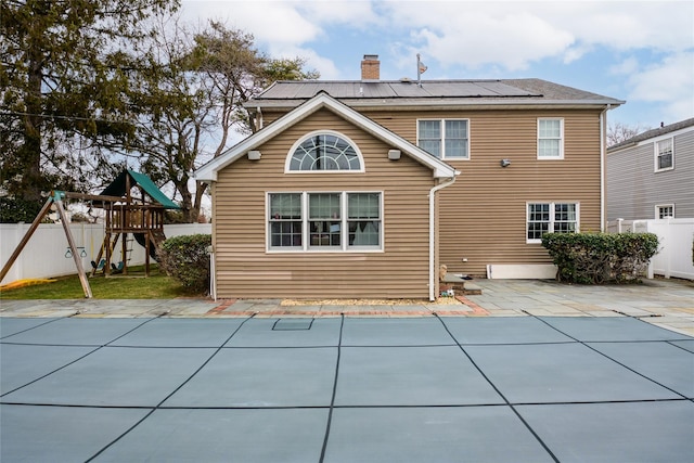 back of house featuring solar panels, a patio area, a playground, and a covered pool