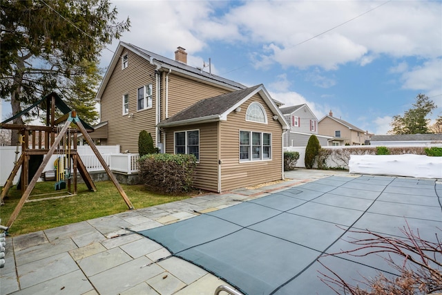 rear view of house featuring a covered pool, a playground, and a patio