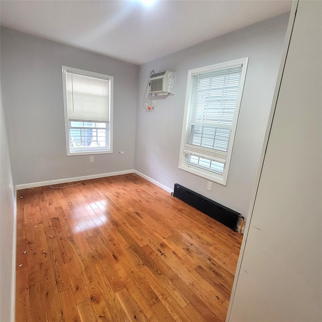 empty room with a baseboard heating unit, light hardwood / wood-style flooring, a wealth of natural light, and an AC wall unit