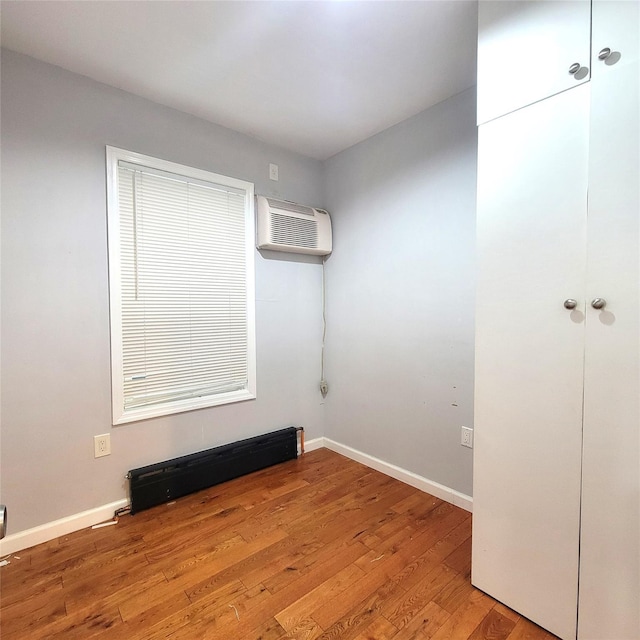 empty room featuring light wood-type flooring, a baseboard radiator, and a wall mounted AC