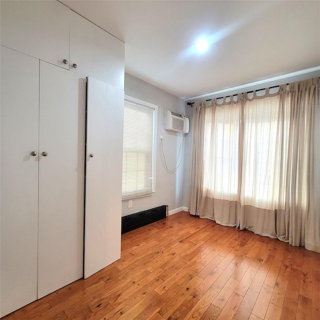 unfurnished bedroom featuring a wall mounted air conditioner, light wood-type flooring, a closet, and multiple windows