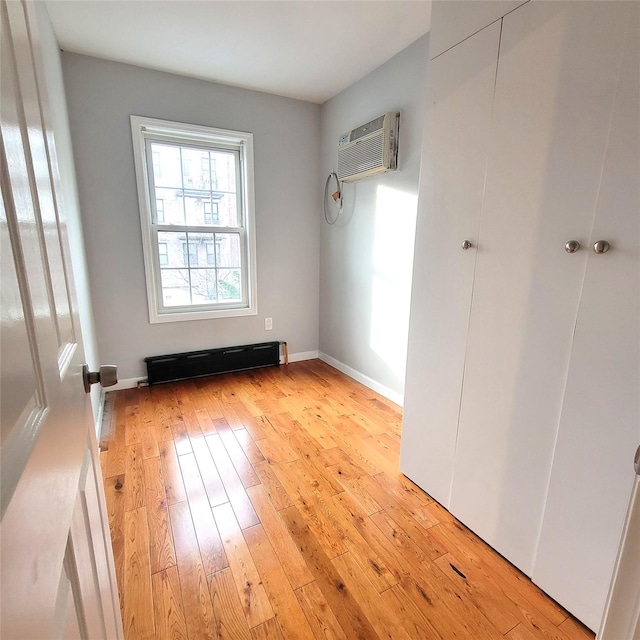 empty room featuring baseboard heating, a wall mounted AC, and light wood-type flooring