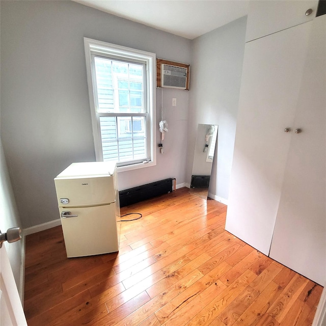 interior space featuring a wall mounted AC, light hardwood / wood-style floors, and a baseboard heating unit