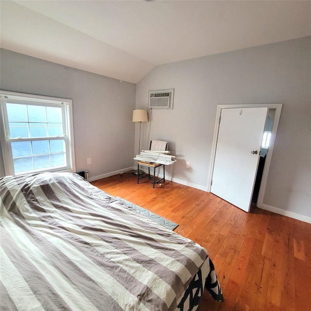 bedroom with a wall mounted air conditioner, lofted ceiling, and light wood-type flooring