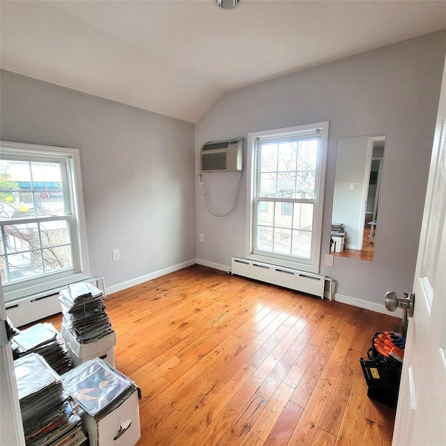 interior space with a baseboard radiator, an AC wall unit, lofted ceiling, and light hardwood / wood-style flooring