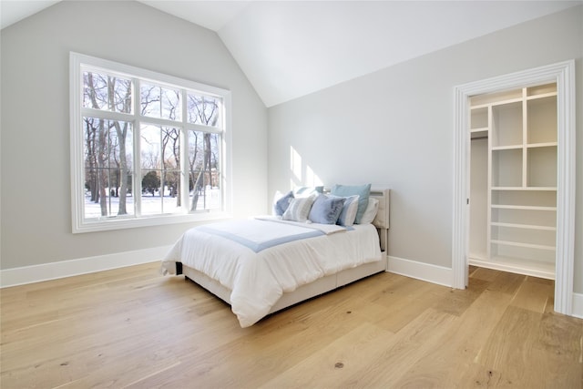 bedroom featuring a spacious closet, vaulted ceiling, and light wood-type flooring