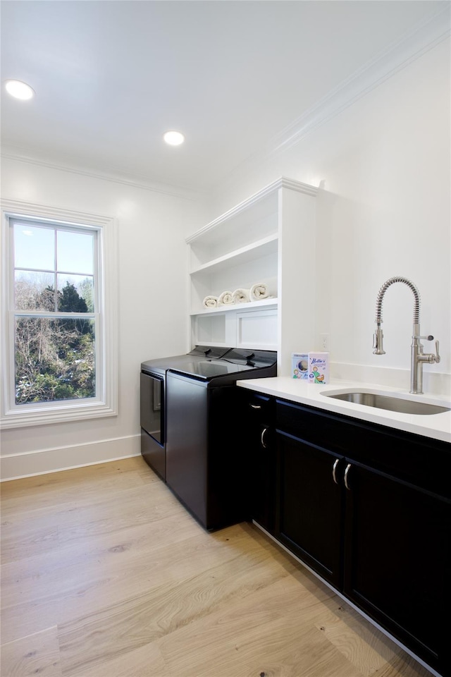 kitchen featuring sink, ornamental molding, washing machine and clothes dryer, and light wood-type flooring