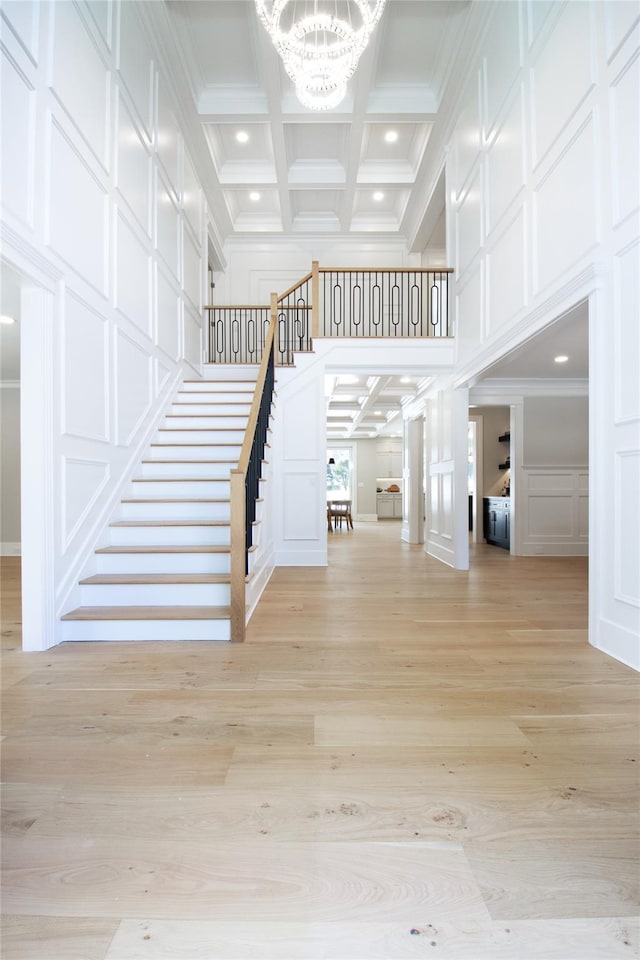 stairs with a chandelier, hardwood / wood-style flooring, ornamental molding, coffered ceiling, and beam ceiling