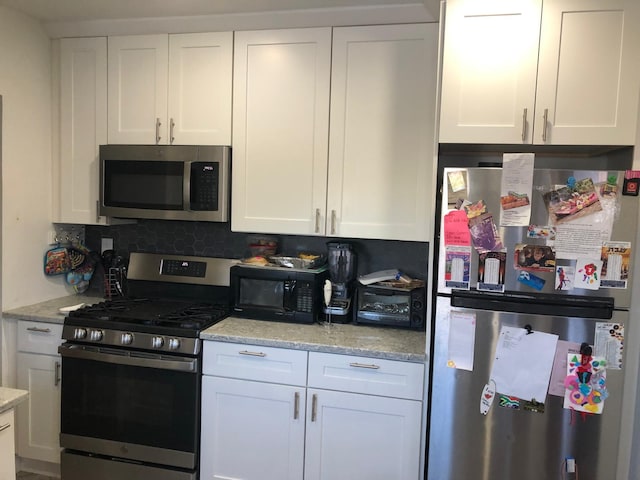 kitchen with decorative backsplash, white cabinetry, light stone countertops, and appliances with stainless steel finishes