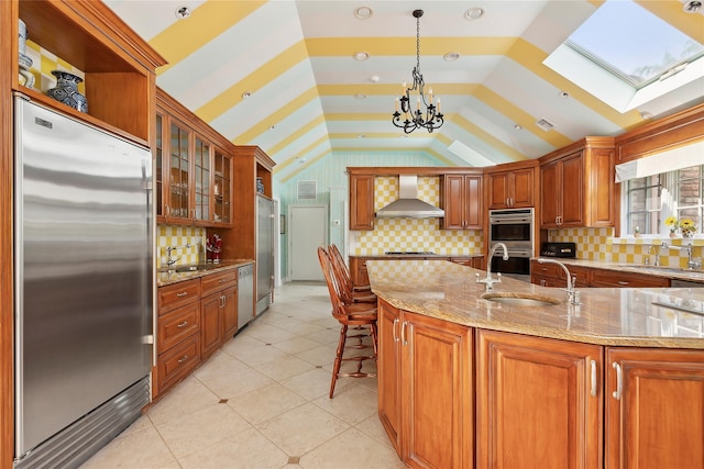 kitchen featuring decorative backsplash, appliances with stainless steel finishes, lofted ceiling with skylight, and wall chimney exhaust hood