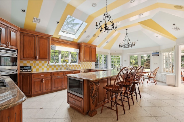 kitchen featuring tasteful backsplash, a skylight, black microwave, a chandelier, and a center island