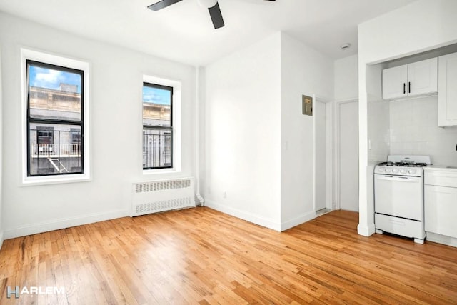 kitchen featuring white gas range oven, radiator, ceiling fan, light hardwood / wood-style flooring, and white cabinets