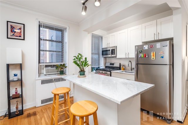 kitchen with a kitchen breakfast bar, radiator, stainless steel appliances, sink, and white cabinetry