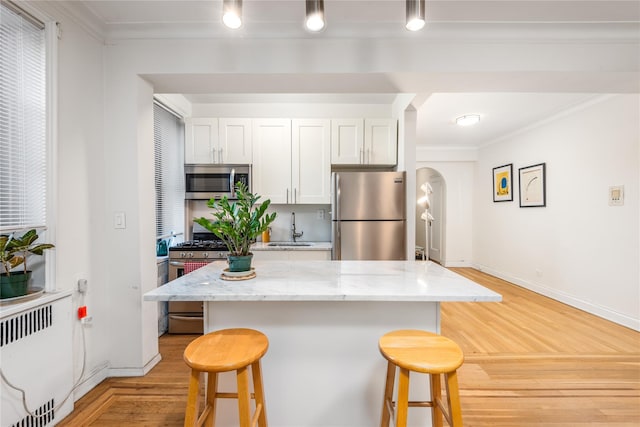 kitchen with white cabinetry, sink, light stone counters, appliances with stainless steel finishes, and ornamental molding