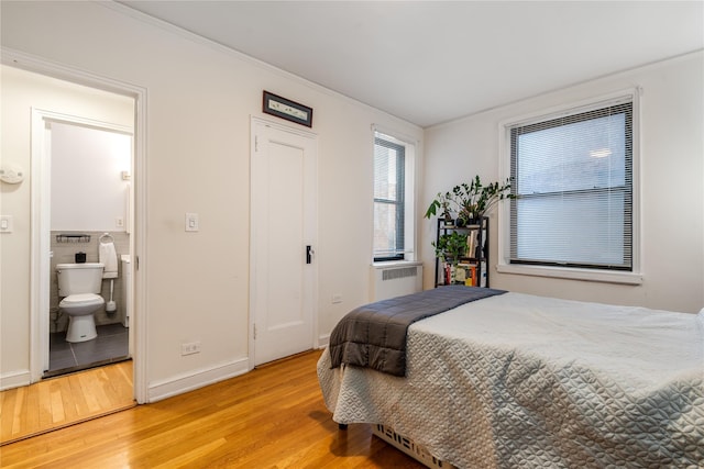 bedroom with connected bathroom, radiator, crown molding, and light hardwood / wood-style flooring