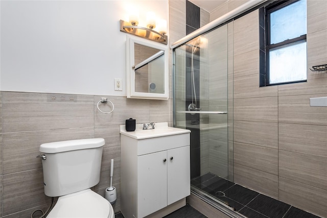 bathroom featuring a shower with door, vanity, tile walls, and toilet