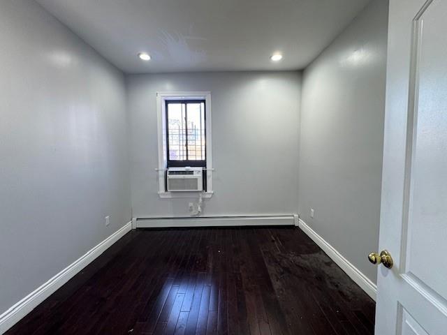 empty room with dark hardwood / wood-style floors and a baseboard heating unit