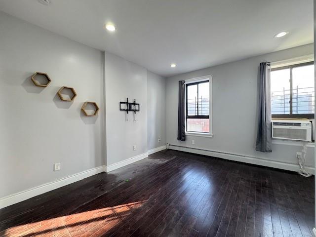 spare room featuring dark hardwood / wood-style floors, baseboard heating, and cooling unit