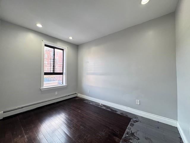 empty room featuring baseboard heating and dark wood-type flooring