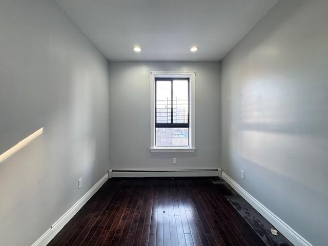 empty room with dark wood-type flooring and a baseboard heating unit