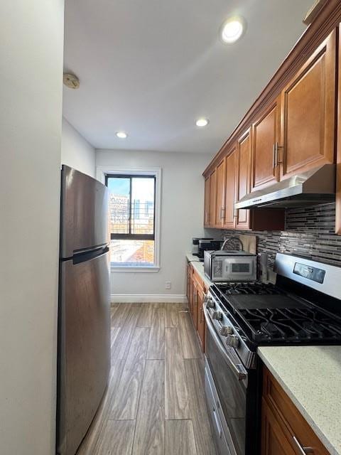 kitchen featuring appliances with stainless steel finishes, backsplash, light hardwood / wood-style flooring, and light stone counters