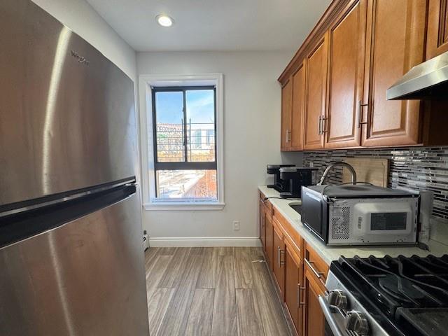 kitchen featuring backsplash, exhaust hood, light hardwood / wood-style flooring, and stainless steel appliances