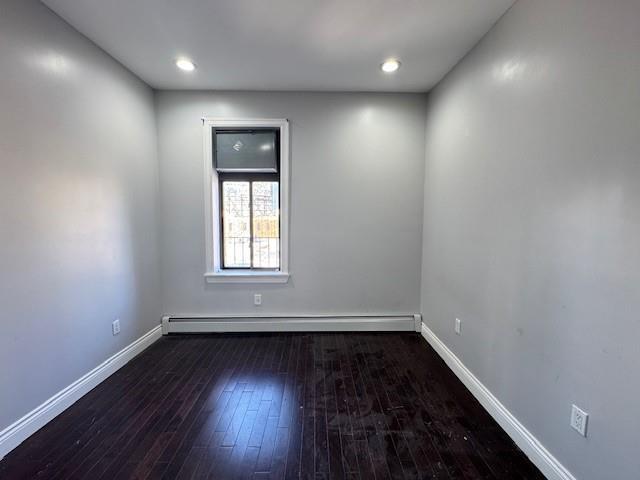 spare room with baseboard heating and dark wood-type flooring