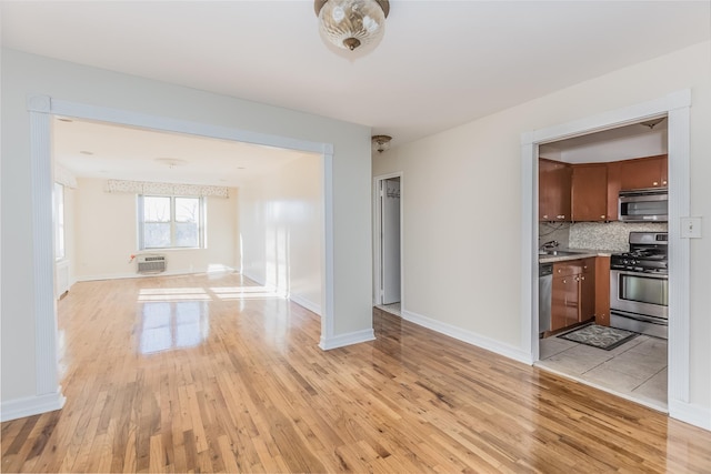 unfurnished living room featuring a wall unit AC, sink, and light wood-type flooring