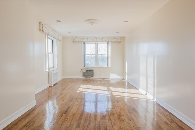 empty room with a wall mounted AC, radiator heating unit, a healthy amount of sunlight, and light hardwood / wood-style floors