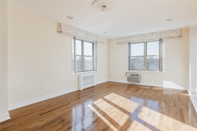 unfurnished room with radiator heating unit, hardwood / wood-style flooring, and an AC wall unit