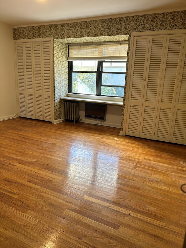 unfurnished bedroom with radiator, two closets, and light wood-type flooring