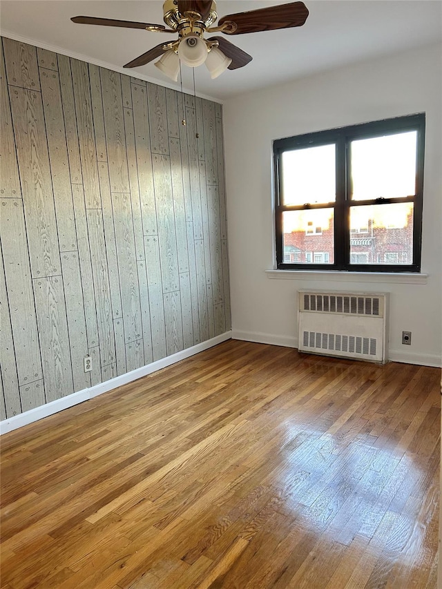 spare room with ceiling fan, light hardwood / wood-style floors, radiator heating unit, and wooden walls