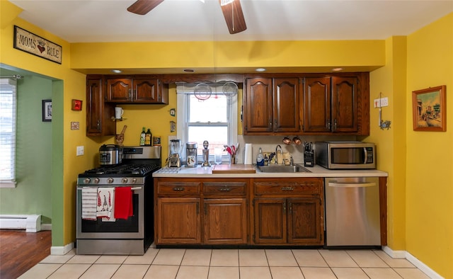 kitchen with ceiling fan, sink, baseboard heating, light tile patterned floors, and appliances with stainless steel finishes