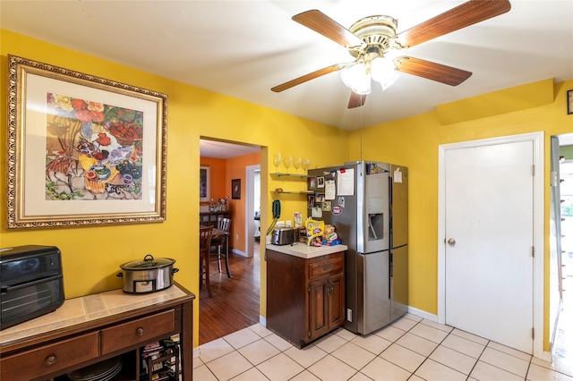 kitchen featuring tile countertops, ceiling fan, dark brown cabinets, light tile patterned flooring, and stainless steel fridge with ice dispenser