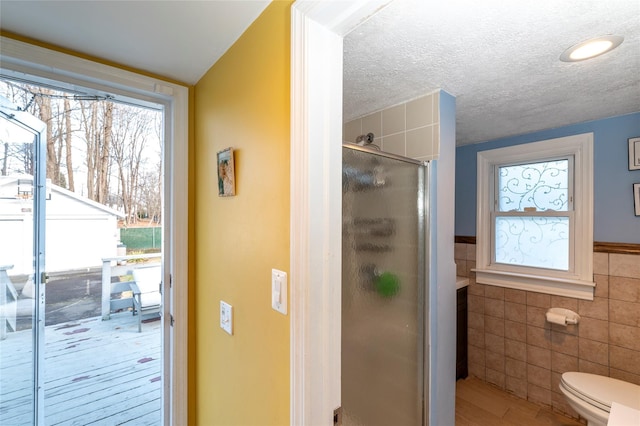 bathroom with a textured ceiling, an enclosed shower, toilet, tile walls, and hardwood / wood-style flooring