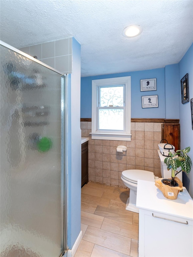 bathroom featuring a textured ceiling, toilet, an enclosed shower, and tile walls