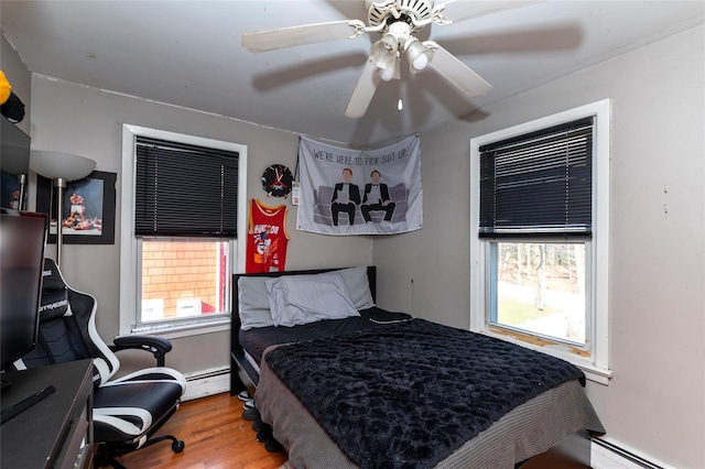 bedroom featuring multiple windows, wood-type flooring, baseboard heating, and ceiling fan