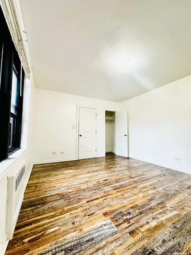 unfurnished bedroom with hardwood / wood-style flooring, radiator heating unit, and multiple windows