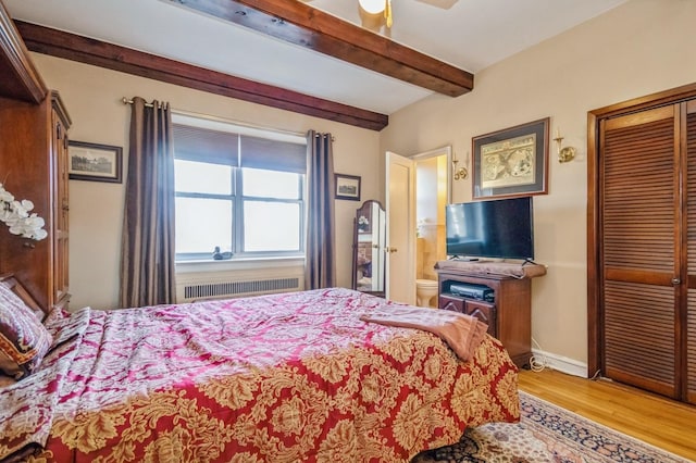 bedroom featuring radiator, ceiling fan, beam ceiling, hardwood / wood-style floors, and a closet