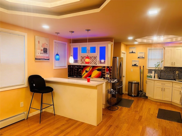 bar with a tray ceiling, light hardwood / wood-style flooring, hanging light fixtures, and a baseboard radiator