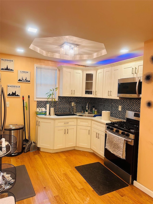 kitchen with a raised ceiling, sink, stainless steel appliances, and light wood-type flooring