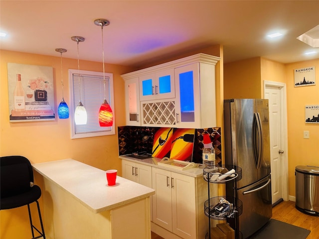 kitchen featuring stainless steel refrigerator, hanging light fixtures, a kitchen breakfast bar, kitchen peninsula, and white cabinets