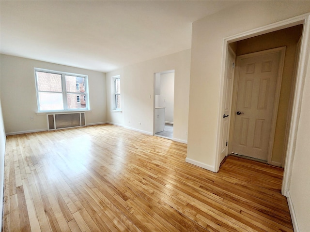 empty room featuring a healthy amount of sunlight, radiator heating unit, and light wood-type flooring